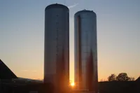 Zwei hohe zylindrische Metallsilos stehen nebeneinander, mit der untergehenden Sonne dahinter, die lange Schatten wirft.