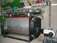 Eine große Industriemaschine mit schwarzem und silbernem Gehäuse, angeschlossen an Rohre und Ventile, steht in einer Fabrik.