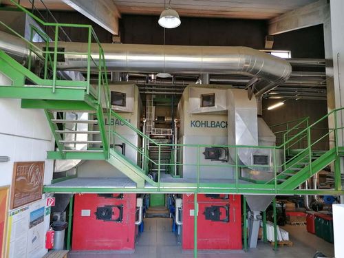 Eine Innenfabrik mit großen roten Kesseln, die mit 'KOHLBACH' und 'L3ACH' beschriftet sind. Die Fabrik hat Metalltreppen und Geländer, große Rohre und mehrere gestapelte Kisten.