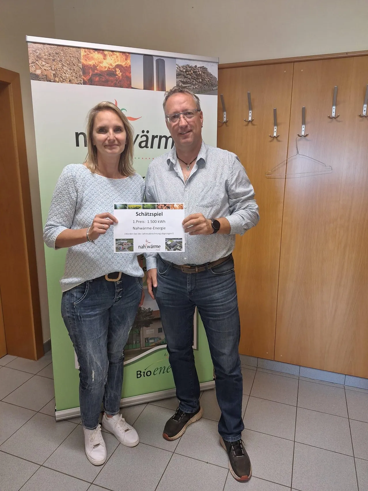 Ein Mann und eine Frau stehen vor einem Banner mit einem Preiszertifikat für 1.500 kWh erneuerbare Energie. Sie lächeln und posieren für ein Foto.