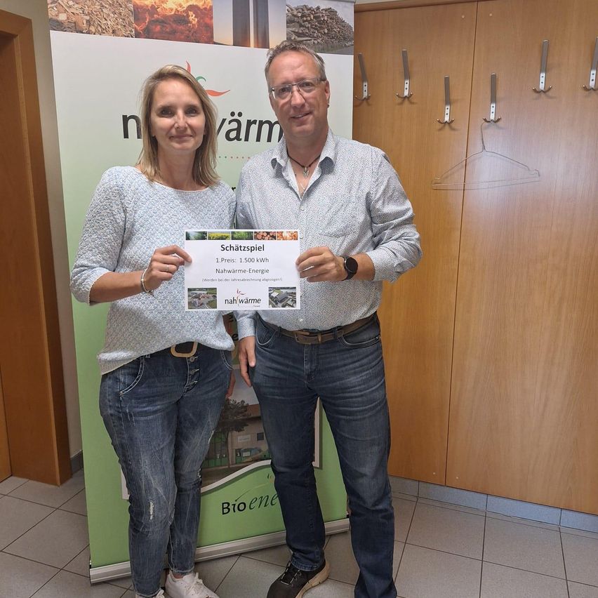 Ein Mann und eine Frau stehen vor einem Banner mit einem Preiszertifikat für 1.500 kWh erneuerbare Energie. Sie lächeln und posieren für ein Foto.