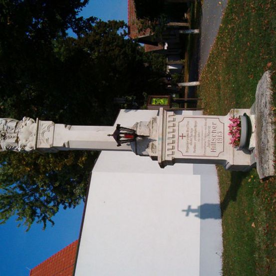 Ein hoher weißer Steinmonument mit komplizierten Schnitzereien und einer Laterne, auf einer Rasenfläche stehend. Es handelt sich wahrscheinlich um einen Gedenkstein.