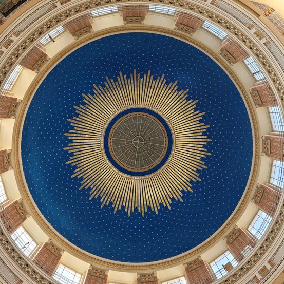 Die Innenkuppel zeigt ein blaues Himmelsdesign mit goldenen Strahlen und einem kreisförmigen Muster. Sie ist von mehreren Fenstern und dekorativen Elementen umgeben.