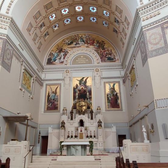 Ein Innenraum einer Kirche mit einem goldenen Altar, umgeben von großen Gemälden an den Wänden. Die Decke ist mit aufwendigen Designs und religiösen Bildern verziert.