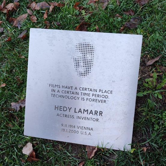 Eine Metallplatte auf Gras zeigt einen Zitat von Hedy Lamarr, Schauspielerin und Erfinderin, geboren 1914 in Wien und gestorben 2000 in den USA.