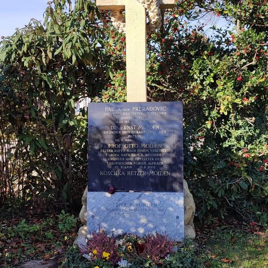 Eine Gedenktafel auf einem Friedhof mit einem Kreuz dahinter. Es steht 'Paula von Preradovic' und 'Ernst Molden'. Unten steht 'Prof. Otto Molden' und weitere Details.