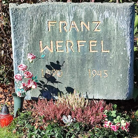 Ein Grabstein für Franz Werfel, geboren 1890 und gestorben 1945, ist von Blumen und Pflanzen umgeben.