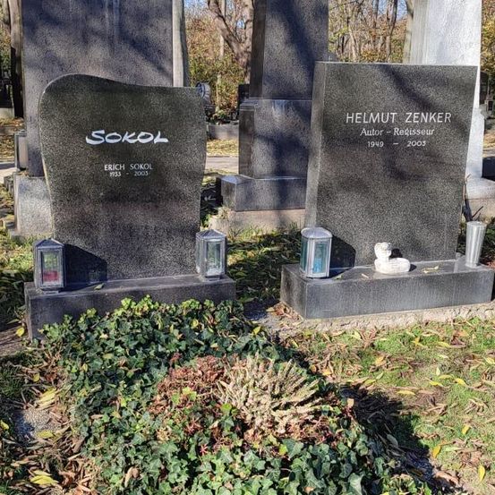 Zwei graue Grabsteine auf einem Friedhof. Links ist der Name 'Erich Sokol' mit den Geburts- und Todesjahren 1913 und 2003 eingraviert. Rechts ist 'Helmut Zenker' mit den Geburts- und Todesjahren 1949 und 2003 eingraviert. Auf den Grabsteinen stehen drei Laternen.