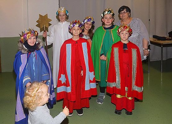 Eine Gruppe von Kindern und Erwachsenen in farbenfrohen Kostümen posiert für ein Foto in einem Raum. Sie halten Requisiten und lächeln.