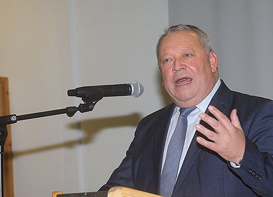 Ein Mann in Anzug und Krawatte spricht in ein Mikrofon und gestikuliert mit der Hand. Das Mikrofon steht auf einem Ständer. Dahinter befindet sich eine weiße Wand.