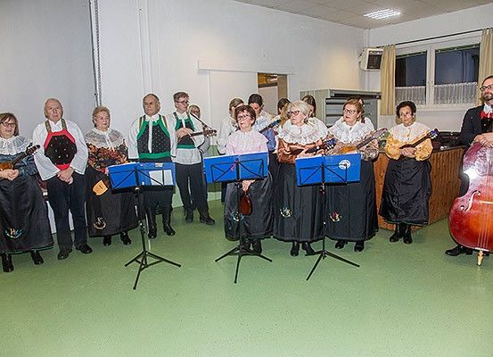 Eine Gruppe von Menschen in traditioneller Kleidung versammelt sich in einem Raum und hält verschiedene Musikinstrumente in den Händen. Sie scheinen eine Aufführung zu absolvieren.