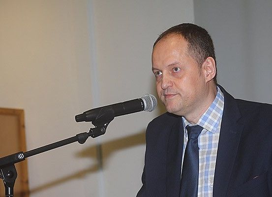 Ein Mann steht vor einem Mikrofon an einem Ständer und hält wahrscheinlich eine Rede in einem Konferenzraum.