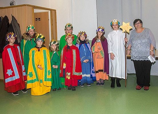 Eine Gruppe von Kindern in verschiedenen Kostümen, möglicherweise für ein Theaterstück, steht in einem Raum. Eine erwachsene Frau mit einem Stern steht rechts.