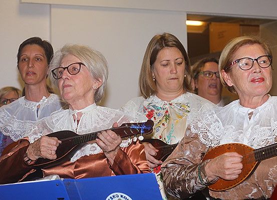 Eine Gruppe älterer Frauen in traditioneller Kleidung spielt Saiteninstrumente in einem Raum.