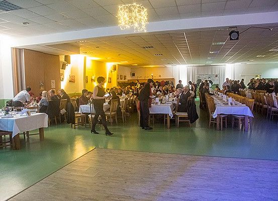 Ein Indoor-Essbereich mit Menschen an Tischen, mit Kellnern, die herumlaufen, und einer von der Decke hängenden Kronleuchter.