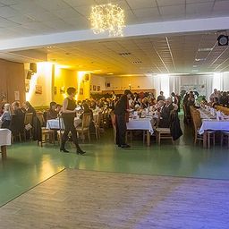 Ein Indoor-Essbereich mit Menschen an Tischen, mit Kellnern, die herumlaufen, und einer von der Decke hängenden Kronleuchter.