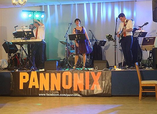 Eine Band tritt auf der Bühne mit einem Banner auf, das Pannonix liest, mit einer Frau, die singt, einem Mann, der Gitarre spielt, und einem anderen Mann am Keyboard.