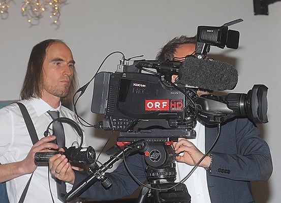 Zwei Männer mit einer Sony ORFD HD-Kamera, einer hält eine Kamera und der andere justiert die Kamera. Sie tragen beide Anzüge und Krawatten.