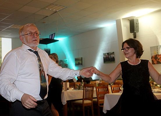 Ein älterer Mann und eine ältere Frau tanzen in einem Restaurant. Sie lächeln und scheinen sich zu amüsieren.