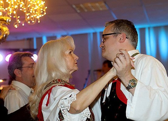 Eine ältere Frau und ein Mann tanzen auf einer Party, mit einer Kristallleuchte und Bühnenlichtern darüber.