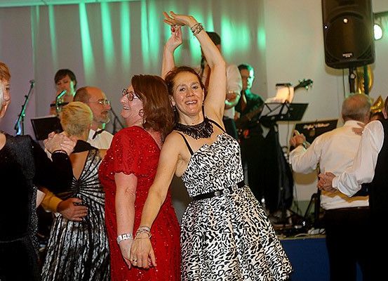 Mehrere Frauen tanzen in einem Raum mit grünen Lichtern und einer Bühne, auf der eine Band spielt.