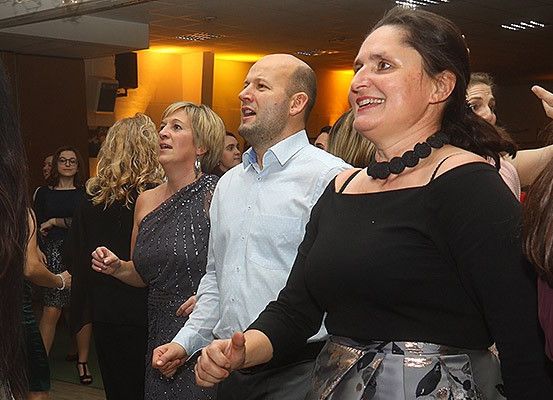 Eine Gruppe von Menschen tanzt in einem schwach beleuchteten Raum, einige mit Lächeln im Gesicht, beleuchtet von warmen gelben Lichtern.