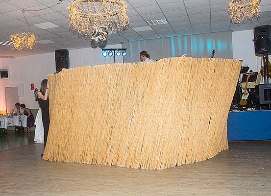 Eine Bühnenaufstellung mit einer großen, dekorativen, bambusartigen Struktur. Ein Mann steht dahinter und eine Frau macht ein Foto. Musikinstrumente und Lautsprecher sind sichtbar.