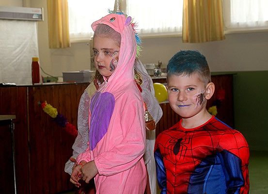 Zwei Kinder in Kostümen stehen eng beieinander, eines verkleidet als Einhorn und das andere als Spider-Man, mit einem Party-Setting im Hintergrund.