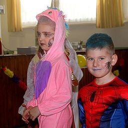 Zwei Kinder in Kostümen stehen eng beieinander, eines verkleidet als Einhorn und das andere als Spider-Man, mit einem Party-Setting im Hintergrund.