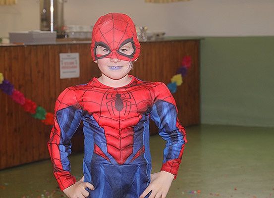 Ein junger Junge in einem roten und blauen Spiderman-Kostüm steht in einem Raum mit einem Holztresen und Dekorationen.