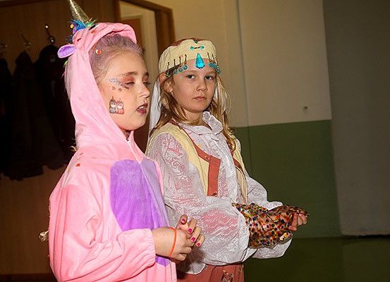 Zwei junge Mädchen in Kostümen stehen in einem Raum. Eine ist als Einhorn gekleidet und die andere in mittelalterlicher Kleidung. Sie halten beide etwas in ihren Händen.
