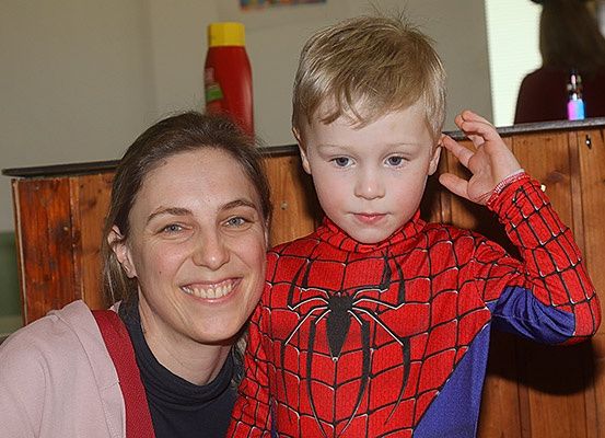 Eine Frau und ein Junge, der als Spider-Man verkleidet ist, stehen nah beieinander und lächeln für ein Foto in einem Raum mit Holzwänden.