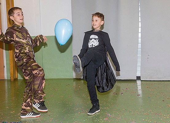 Zwei Jungen spielen mit einem blauen Ballon, einer in Camouflage und der andere in einem Star Wars-Shirt, mit Konfetti auf dem Boden.