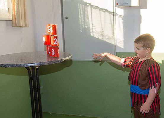 Ein junger Junge in einem Kostüm steht vor einem Tisch mit gestapelten Bechern darauf.