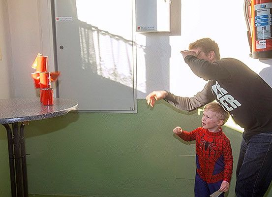 Ein Mann und ein junger Junge in einem Spiderman-Kostüm befinden sich in einem Raum mit einem Feuerlöscher und einem Tisch mit roten Bechern.