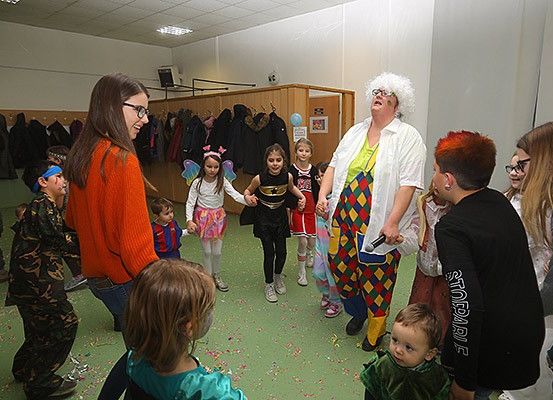 Eine Gruppe von Kindern und Erwachsenen in einem Raum mit einem Clowncharakter, der tanzt und lacht. Einige Kinder tragen Kostüme.