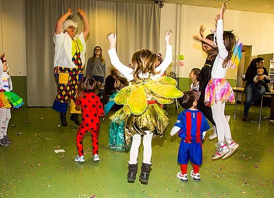 Eine Gruppe von Kindern in Kostümen tanzt in einem Raum mit einer Person in einem Clown-Kostüm.