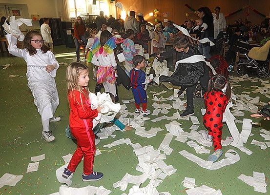Kinder in Kostümen werfen Papierstücke aufeinander in einem überfüllten Raum. Sie veranstalten einen Papierkampf.