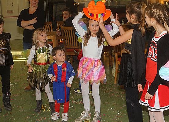 Eine Gruppe von Kindern in Kostümen und Hüten steht zusammen in einem Raum. Ein Mädchen trägt einen Kürbis-Hut.