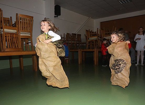 Zwei Mädchen springen in Bohnensäcken in einem Raum mit Stühlen und grünem Boden. Eine hält einen Bohnensack mit Logo.