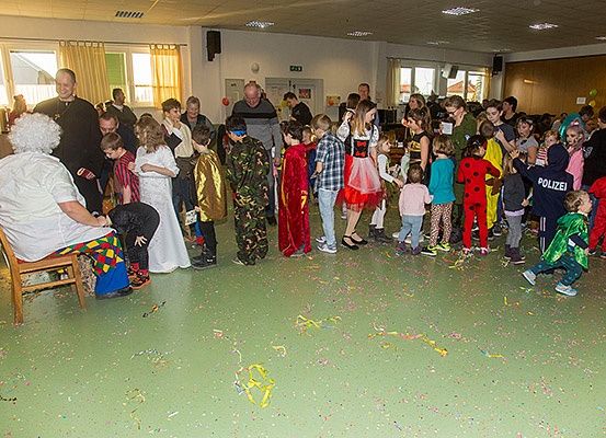 Eine Gruppe von Kindern und Erwachsenen in einem Raum mit Konfetti. Viele tragen Kostüme, darunter ein Marienkäfer, ein Soldat und ein Polizist.