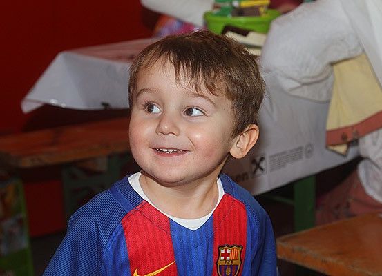 Ein junger Junge lächelt und posiert für ein Foto in einem Raum mit einer roten Wand. Er trägt ein blaues und rotes Trikot mit dem Barcelona-Logo.