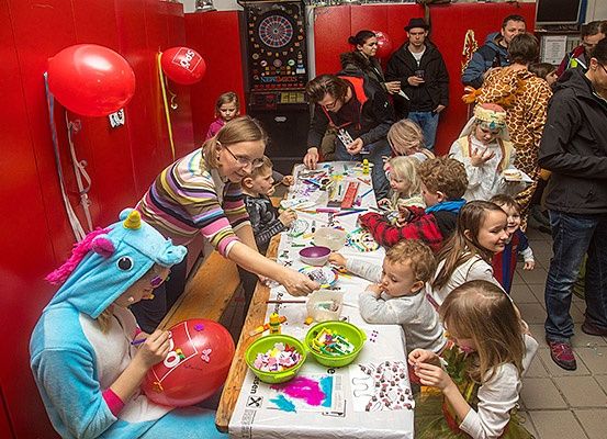 Eine Gruppe von Menschen, einschließlich Kindern, ist um einen Tisch mit Kunstmaterialien und Ballons versammelt. Einige sind in Kostümen gekleidet und andere beobachten.