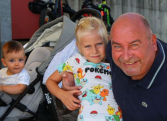 Ein Mann und ein Mädchen stehen eng beieinander, während ein Baby in einem Kinderwagen sitzt. Das Mädchen trägt ein Pokemon-Shirt und der Mann ein blaues Poloshirt.