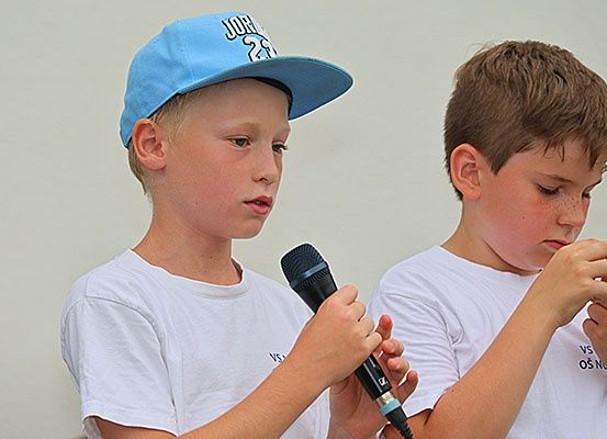 Zwei Jungen, einer trägt einen blauen Hut mit dem Wort 'JOR' und der andere ein Mikrofon, stehen nebeneinander. Sie tragen beide weiße T-Shirts.
