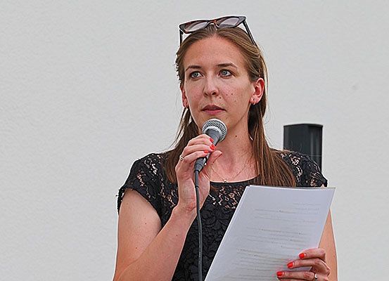 Eine Frau mit einer Brille auf dem Kopf spricht in ein Mikrofon, während sie ein Papier in der Hand hält.