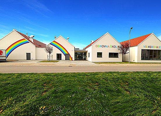 Drei Gebäude mit roten Dächern und einem großen Regenbogen an der Wand. Die Gebäude sind wahrscheinlich Schulen.