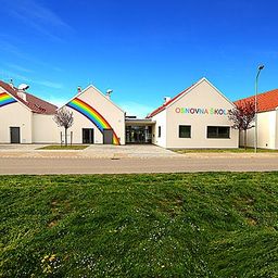 Drei Gebäude mit roten Dächern und einem großen Regenbogen an der Wand. Die Gebäude sind wahrscheinlich Schulen.