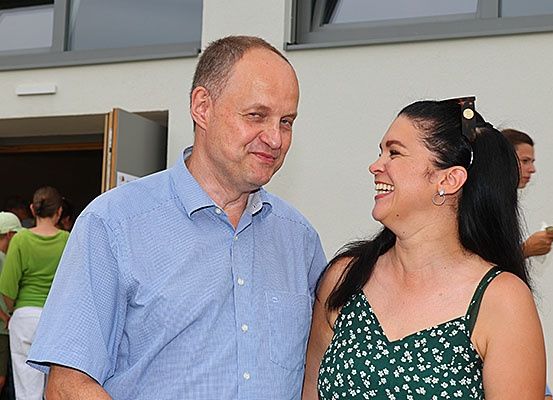 Ein Mann und eine Frau stehen nah beieinander und lächeln, während andere hinter ihnen in einem Raum mit offener Tür stehen.