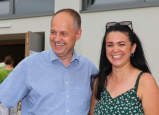 Ein Mann und eine Frau lächeln und posieren für ein Foto vor einem Gebäude.
